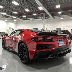 Un Chevrolet Corvette rojo brillante con detalles en negro, aparcado en un taller de detallado, en el que destacan su agresivo diseño trasero, los cuatro tubos de escape y una matrícula de Minnesota.