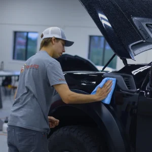 Un técnico que lleva una camiseta de Bravo Protection Products limpia el guardabarros de una camioneta negra con un paño de microfibra azul.