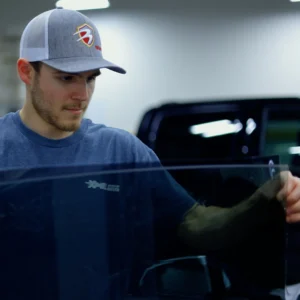 Un hombre que lleva una gorra de Bravo Protection Products coloca una lámina de Tintado de Vidrios de automóvil Tintado de Vidrios la marca Tintado de Vidrios .